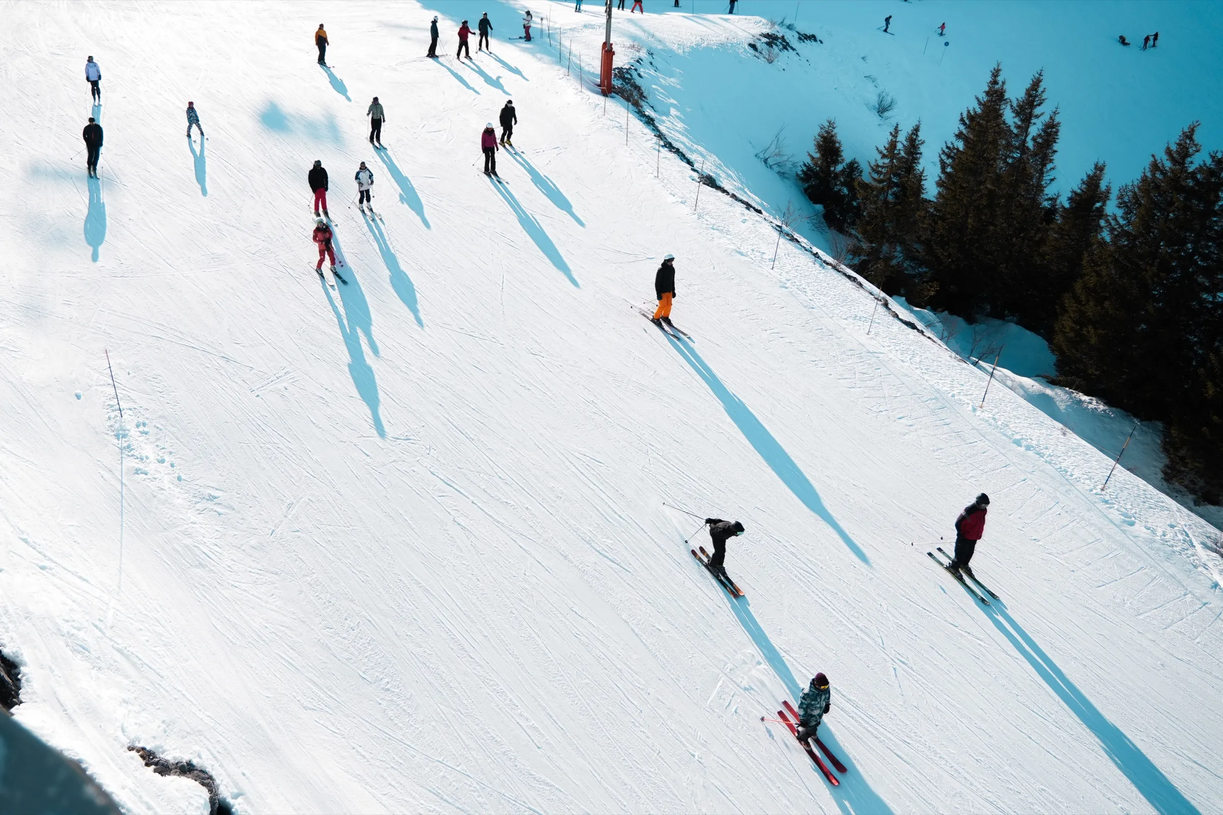 Skiers and instructors spread across a piste in long afternoon shadow.