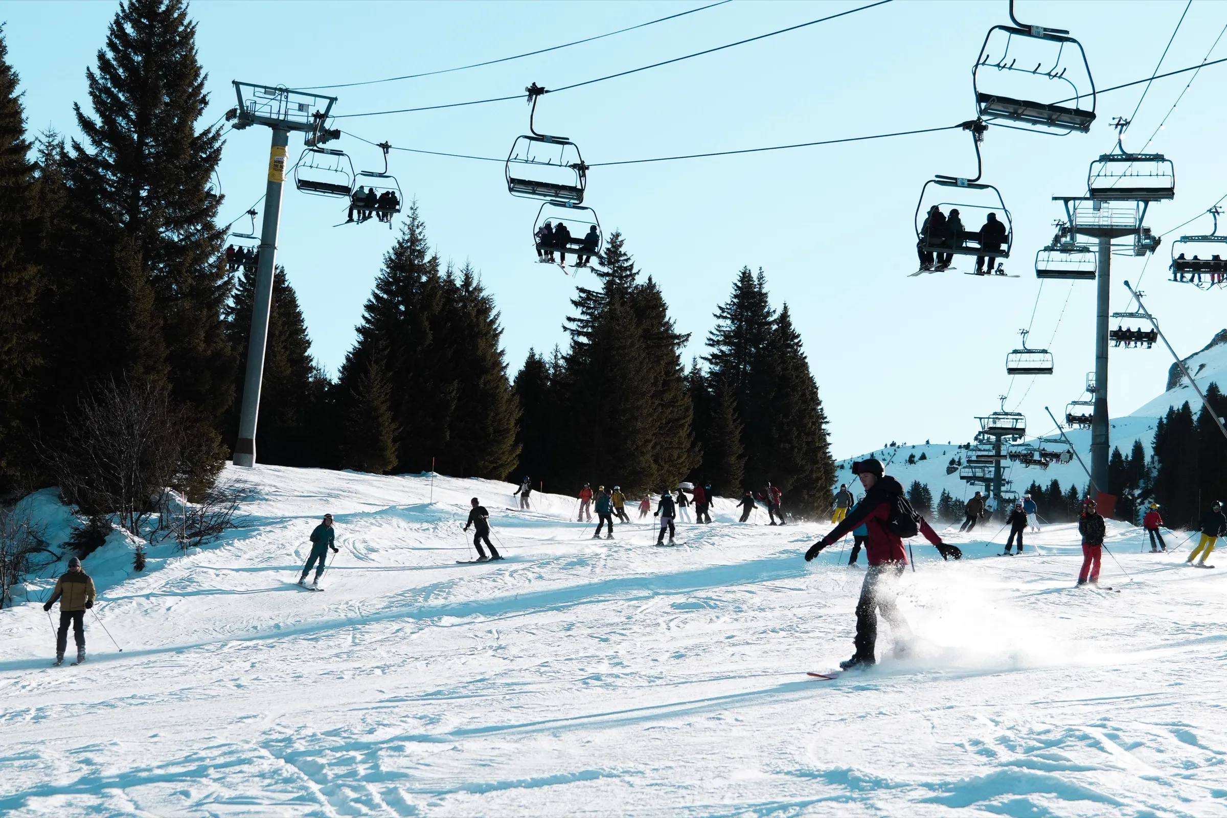 A skier under a chairlift on a busy piste.